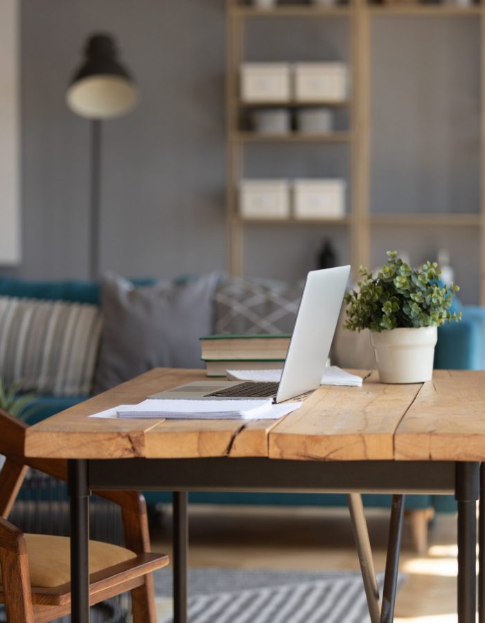 Empty wooden loft desk with open modern laptop and book on, cozy living room interior design of student or freelance employee, comfortable domestic workplace with table and computer in apartment