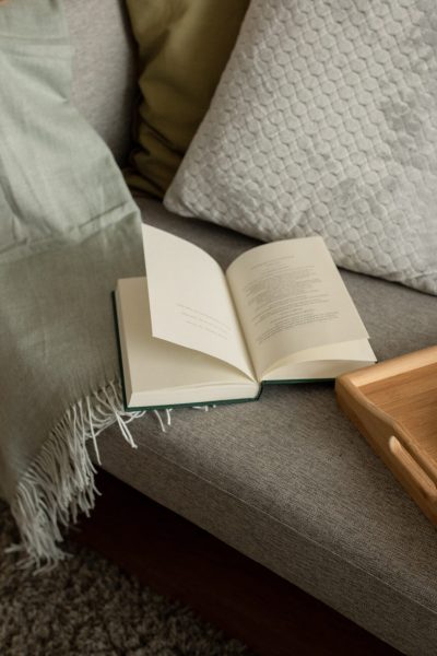 Book, tray with food and coffee cup on sofa in living room interior at evening, top view. Hobbies, literature in free time, cozy, comfort at home, study, education and fairytale, nobody