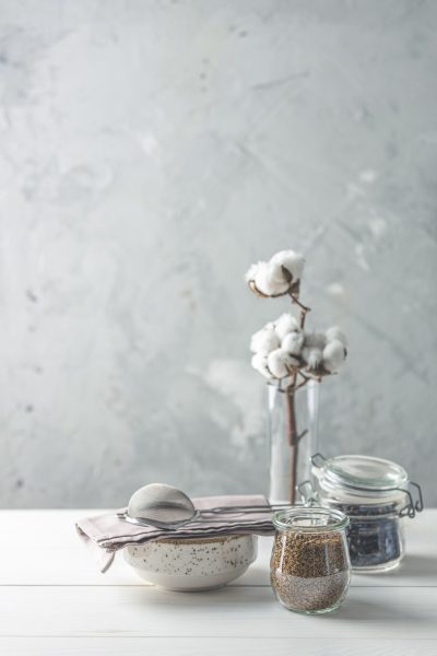 Coffee beans and instant coffee in glass jars, cotton flowers and kitchenware on white wooden table with grey concrete wall at background. Details of still life in the home interior. Cosy concept.